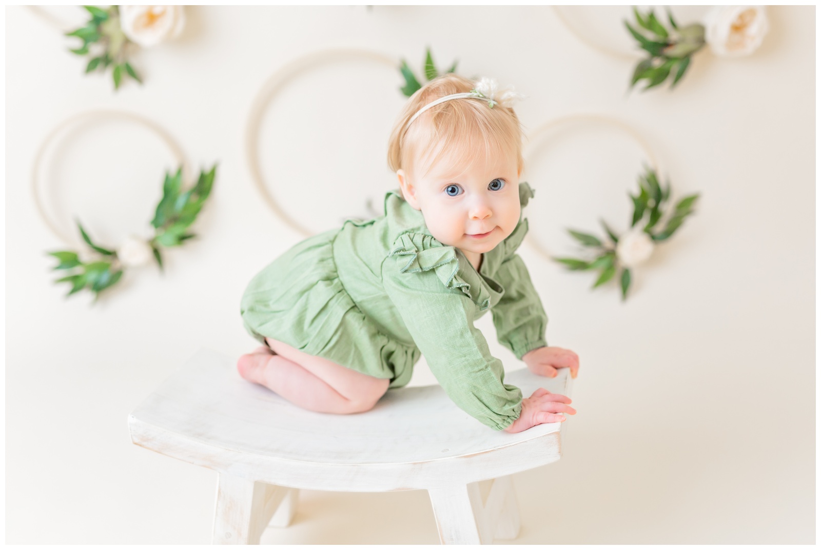 1 year old in green romper on stool, studio session, organic floral hoops in background