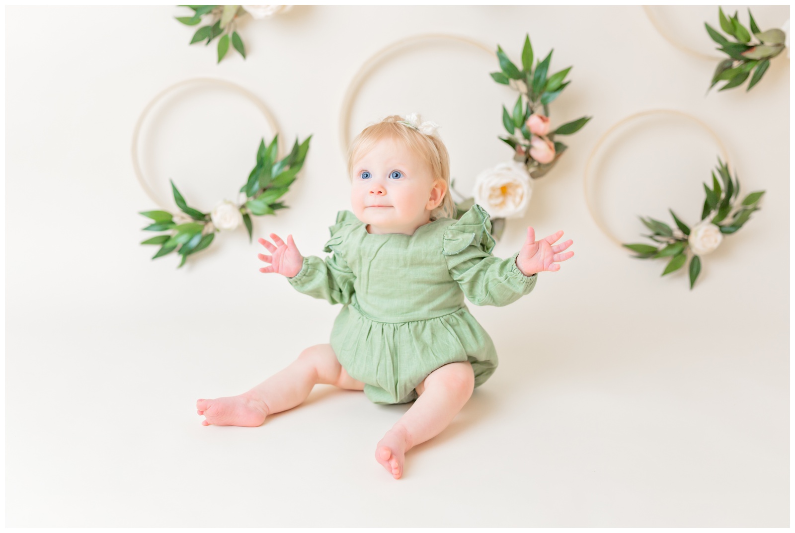 1 year old in green romper with hands outstretched, cake smash session, organic floral hoops in background