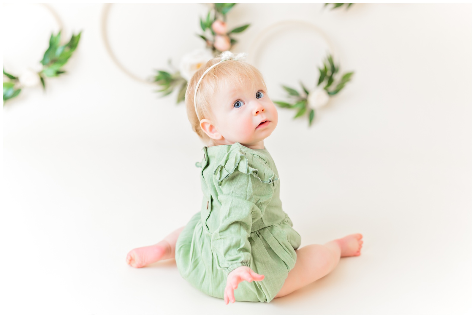 1 year old in green romper, studio session. organic floral hoops in background