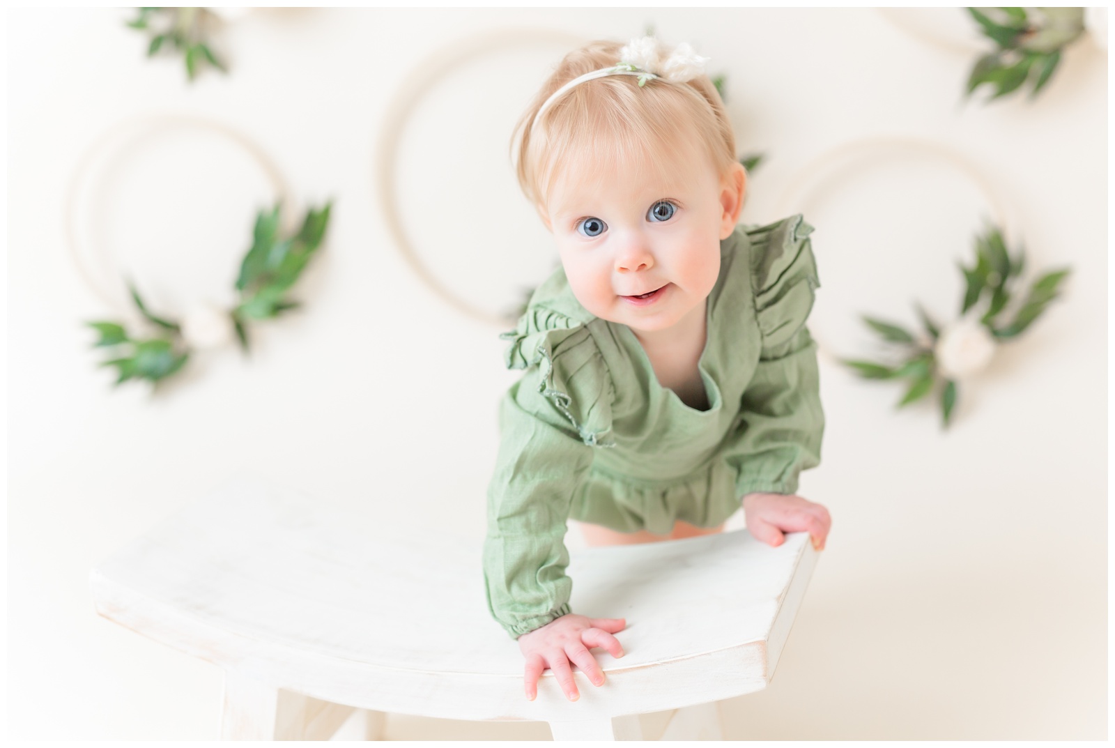 1 year old in green romper on stool, cake smash session, organic floral hoops in background