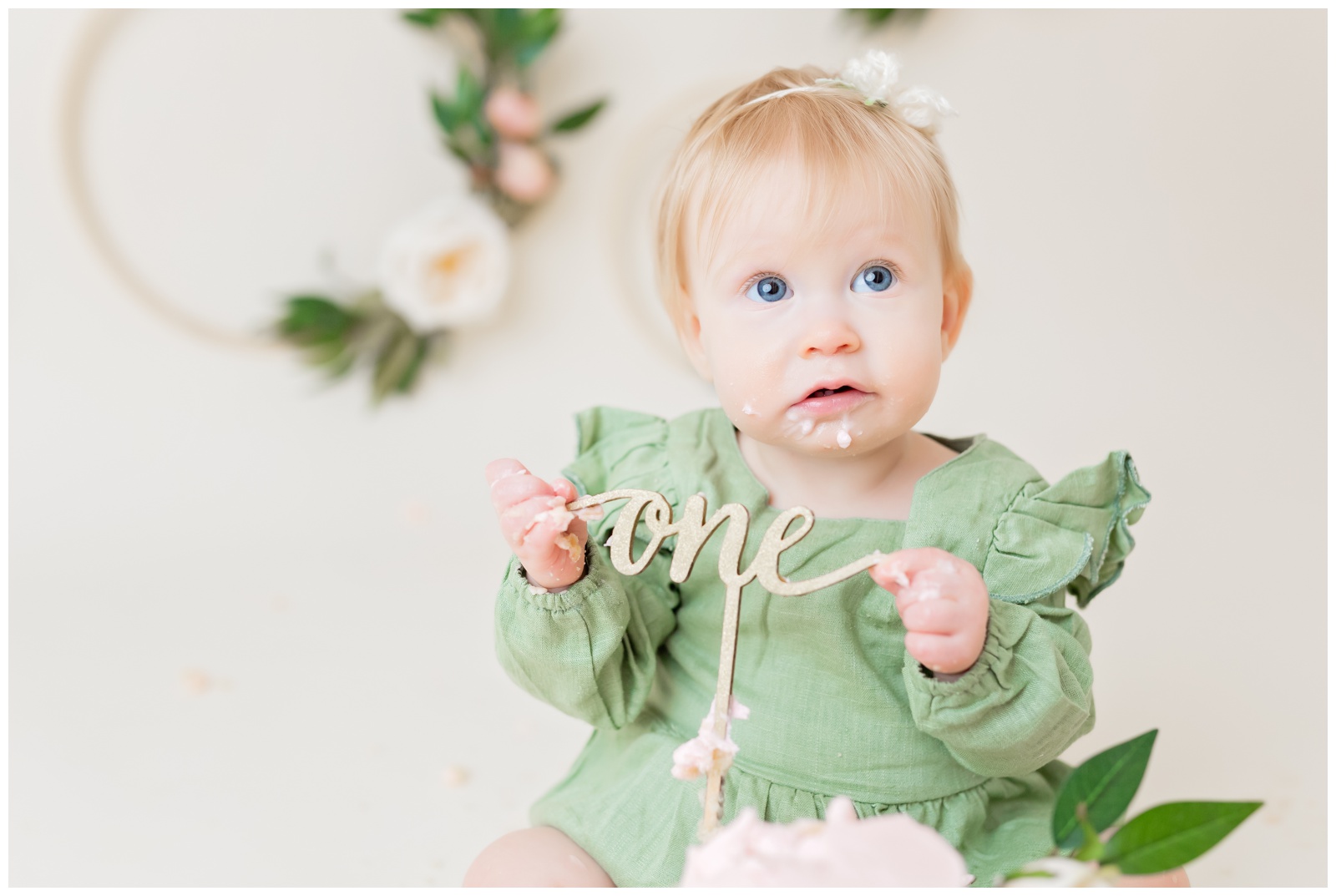 1 year old holding cake topper, organic floral hoops in background, cake smash session